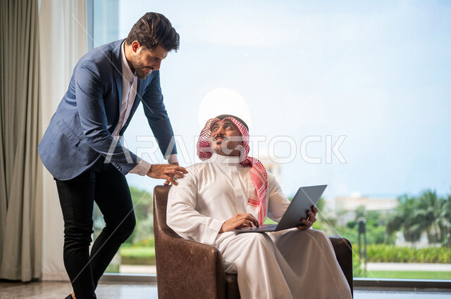 رجل أعمال عربي سعودي خليجي مع رجل أعمال عربي يرتدي البدلة الرسمية في مقر الشركة، إستخدام جهاز الحاسوب المحمول، مهن ووظائف سعودية، شركة سعودية، بيئة عمل، زملاء عمل، الشراكة والتعاون، إجتماع عمل، مناقشة ومتابعة الأعمال, تحقيق استراتيجيات العمل 