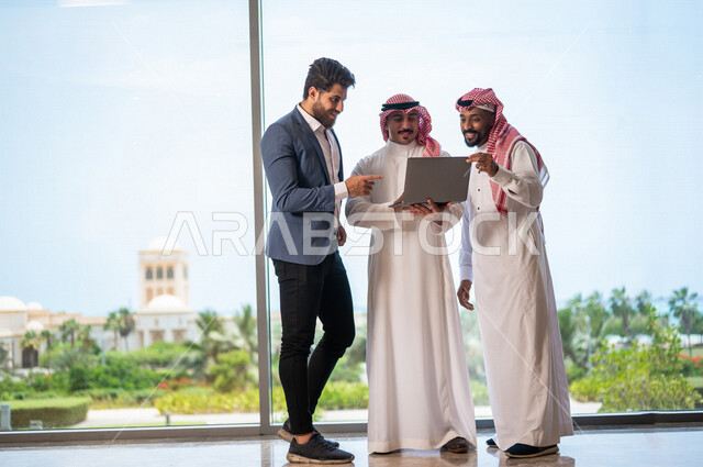 فريق عمل سعودي ورجل بالبدلة الرسمية في مقر الشركة، إستخدام جهاز الحاسوب المحمول، متابعة مهام العمل، شركة سعودية، بيئة عمل سعوديه، زملاء عمل، الشراكة والتعاون، إجتماع عمل، مناقشة ومتابعة الاعمال, تحقيق استراتيجيات العمل, شركات عربيه سعوديه خليجيه 
