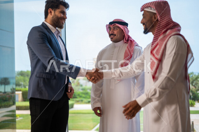 رجل أعمال عربي سعودي خليجي يرتدي الزي السعودي يصافح رجل أعمال عربي يرتدي البدلة الرسمية، الإتفاق على المشاريع التجارية، صفقة عمل جديده, شركاء عمل، التعاون بين الشركات، بيئة عمل سعوديه، إتفاقية عمل, شركات عربيه سعوديه خليجيه في المملكه العربيه السعوديه