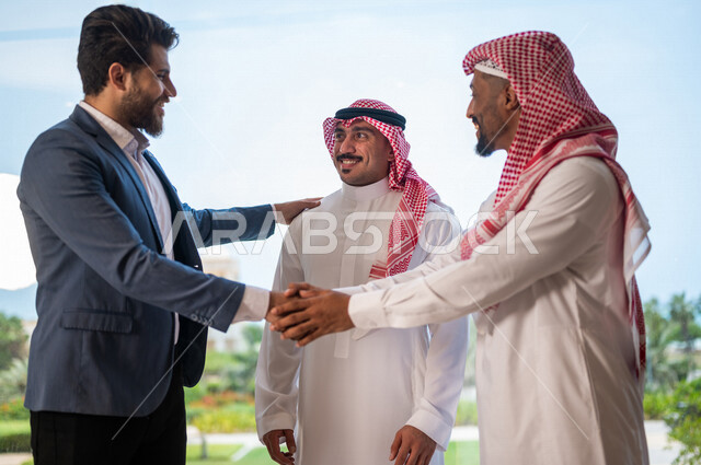 رجل أعمال عربي سعودي خليجي يرتدي الزي السعودي يصافح رجل أعمال عربي يرتدي البدلة الرسمية، الإتفاق على المشاريع التجارية، صفقة عمل جديده, شركاء عمل، التعاون بين الشركات، بيئة عمل سعوديه، إتفاقية عمل, شركات عربيه سعوديه خليجيه في المملكه العربيه السعوديه