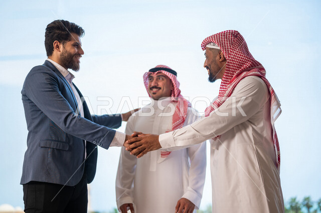 رجل أعمال عربي سعودي خليجي يرتدي الزي السعودي يصافح رجل أعمال عربي يرتدي البدلة الرسمية، الإتفاق على المشاريع التجارية، صفقة عمل جديده, شركاء عمل، التعاون بين الشركات، بيئة عمل سعوديه، إتفاقية عمل, شركات عربيه سعوديه خليجيه في المملكه العربيه السعوديه