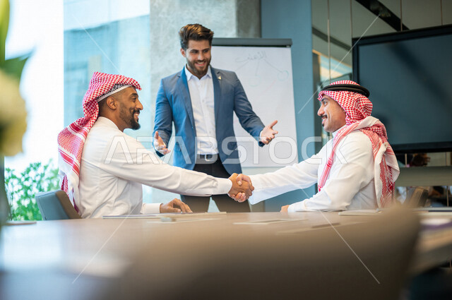 رجلا أعمال عربيان خليجيان سعوديان يتصافحان في غرفة الإجتماعات داخل مقر الشركة، إتفاقية عمل جديده، صفقة عمل, التعاون بين الشركات, مهن ووظائف سعودية، شركة سعودية، زملاء عمل، إجتماع عمل، مناقشة ومتابعة أهداف الشركة 