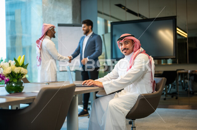 رجل أعمال عربي خليجي سعودي يصافح رجل أعمال يرتدي البدلة الرسمية في غرفة الإجتماعات داخل مقر الشركة، إتفاقية عمل جديده، صفقة عمل, التعاون بين الشركات, مهن ووظائف سعودية، شركة سعودية، زملاء عمل، إجتماع عمل، مناقشة ومتابعة أهداف الشركة 