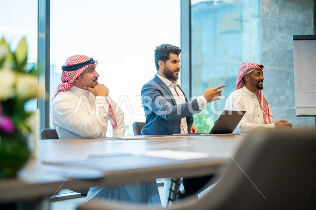 فريق عمل سعودي ورجل بالبدلة الرسمية في غرفة الإجتماعات داخل مقر الشركة، إستخدام جهاز الحاسوب المحمول، مهن ووظائف سعودية، شركة سعودية، بيئة عمل، زملاء عمل، ورشة أعمال، الشراكة والتعاون، إجتماع عمل، مناقشة ومتابعة الأعمال, تحقيق استراتيجيات العمل
