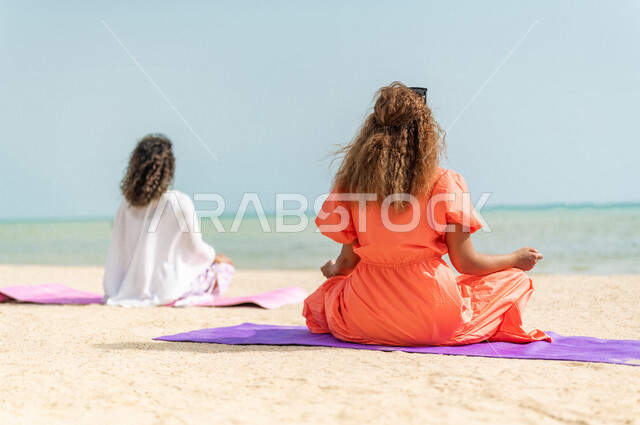 صورة من الخلف لشابتان عربيتان خليجيتان سعوديتان تمارسان رياضة اليوغا التأملية على شاطيء بحر جدة، ممارسة نشاط رياضي، أنشطة و تمارين رياضية، التأمل والاسترخاء، الرياضة والنشاط البدني، تمارين اللياقة البدنية، أسلوب حياة صحي، لياقة ورشاقة