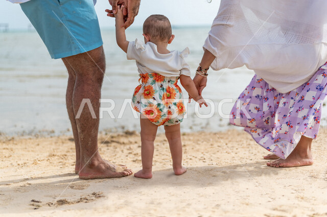 صورة من الخلف لعائلة عربية خليجية سعودية في عطلة صيفية على شاطئ بحر جدة السياحي، المشي على رمل شاطئ البحر، الاستمتاع بالاجازة الصيفية، أجواء عائلية سعيدة، مفهوم الأسرة السعيدة، قضاء نشاطات ترفيهية عائلية، العطلة الصيفية