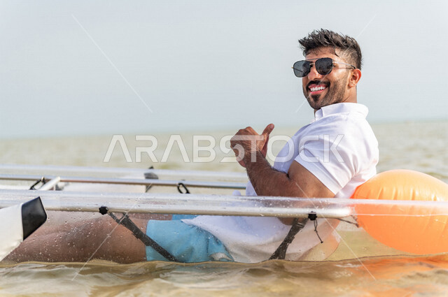 صورة مقربة لرجل عربي خليجي سعودي يرتدي النظارة الشمسية ويجلس داخل قارب قارب التجديف المائي في بحر جدة السياحي، قارب التجديف البلاستيكي الشفاف، انشطة ترفيهية، الاستمتاع بالاجازة الصيفية، ايماءات وجه مبتسمة، القبول والموافقة، سياحة وإستجمام، العطلة الصيفية