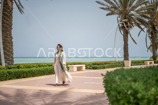 A Saudi Arabian Gulf woman practicing walking in the Jeddah Corniche promenade, a tourist beach, outdoor physical activity, hiking in Jeddah, the waterfront of Jeddah