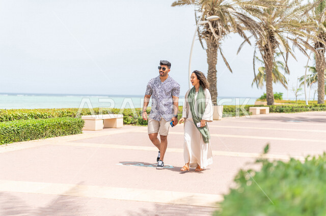 رجل وإمرأه عربيان سعوديان خليجيان يمارسان رياضة المشي في ممشى كورنيش جده, دردشه ومحادثات, شاطيء سياحي, نشاط بدني في الهواء الطلق, التنزه في جده, الواجهه البحريه لمدينة جده