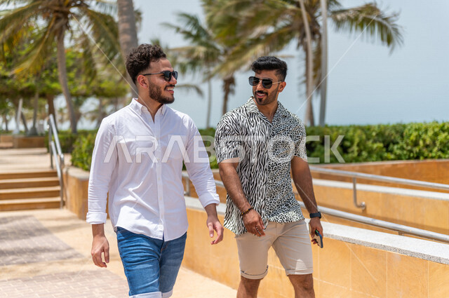 صديقان عربيان سعوديان خليجيان يمارسان رياضة المشي في ممشى كورنيش جده, شاطيء سياحي, نشاط بدني في الهواء الطلق, التنزه في جده, دردشة ومحادثات, الإستمتاع مع الأصدقاء, الواجهه البحريه لمدينة جده