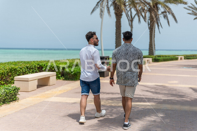 صديقان عربيان سعوديان خليجيان يمارسان رياضة المشي في ممشى كورنيش جده, شاطيء سياحي, نشاط بدني في الهواء الطلق, التنزه في جده, دردشة ومحادثات, الإستمتاع مع الأصدقاء, الواجهه البحريه لمدينة جده