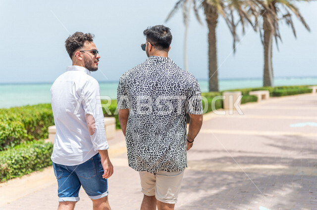 صديقان عربيان سعوديان خليجيان يمارسان رياضة المشي في ممشى كورنيش جده, شاطيء سياحي, نشاط بدني في الهواء الطلق, التنزه في جده, دردشة ومحادثات, الإستمتاع مع الأصدقاء, الواجهه البحريه لمدينة جده