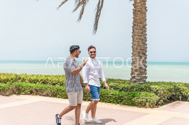 صديقان عربيان سعوديان خليجيان يمارسان رياضة المشي في ممشى كورنيش جده, شاطيء سياحي, نشاط بدني في الهواء الطلق, التنزه في جده, دردشة ومحادثات, الإستمتاع مع الأصدقاء, الواجهه البحريه لمدينة جده