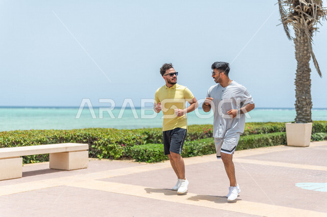 صديقان عربيان سعوديان خليجيان يمارسان رياضة الجري, الصحه واللياقه الجسديه, ممارسة رياضة المشي في ممشى كورنيش جده, شاطيء سياحي, نشاط بدني في الهواء الطلق, التنزه في جده, رياضة الصباح, الواجهه البحريه لمدينة جده