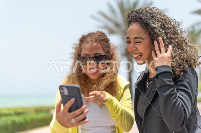 صديقتان عربيتان سعوديتان خليجيتان في ممشى كورنيش جده, إستخدام الهاتف المحمول, التواصل الإجتماعي, شاطيء سياحي, التنزه في جده, دردشة ومحادثات, الإستمتاع مع الأصدقاء, الواجهه البحريه لمدينة جده