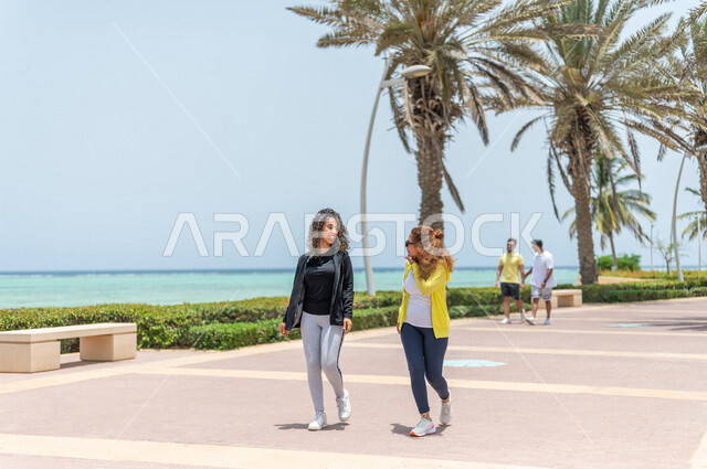 صديقتان عربيتان سعوديتان خليجيتان تمارسان رياضة المشي في ممشى كورنيش جده, شاطيء سياحي, نشاط بدني في الهواء الطلق, التنزه في جده, دردشة ومحادثات, الإستمتاع مع الأصدقاء, الواجهه البحريه لمدينة جده