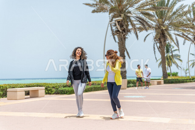 صديقتان عربيتان سعوديتان خليجيتان تمارسان رياضة المشي في ممشى كورنيش جده, شاطيء سياحي, نشاط بدني في الهواء الطلق, التنزه في جده, دردشة ومحادثات, الإستمتاع مع الأصدقاء, الواجهه البحريه لمدينة جده