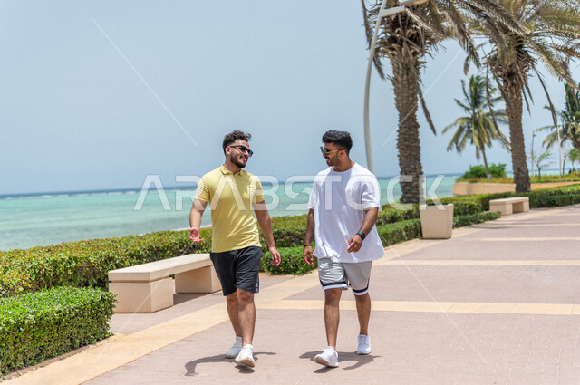 صديقان عربيان سعوديان خليجيان يمارسان رياضة المشي في ممشى كورنيش جده, شاطيء سياحي, نشاط بدني في الهواء الطلق, التنزه في جده, دردشة ومحادثات, الإستمتاع مع الأصدقاء, الواجهه البحريه لمدينة جده
