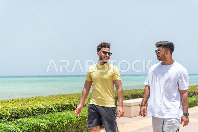 صديقان عربيان سعوديان خليجيان يمارسان رياضة المشي في ممشى كورنيش جده, شاطيء سياحي, نشاط بدني في الهواء الطلق, التنزه في جده, دردشة ومحادثات, الإستمتاع مع الأصدقاء, الواجهه البحريه لمدينة جده