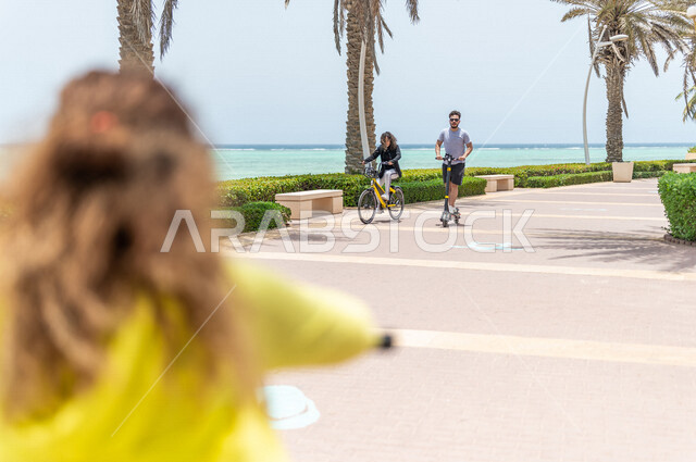 مجموعه من الأصدقاء العرب السعوديون الخليجيون يقومون بركوب السكوتر الكهربائي والدراجه الهوائيه, ممارسة وسائل ترفيهيه في ممشى كورنيش جده, الواجهه البحريه لمدينة جده, مشاركة الأنشطه الترفيهيه مع الأصدقاء, السياحه في السعوديه 