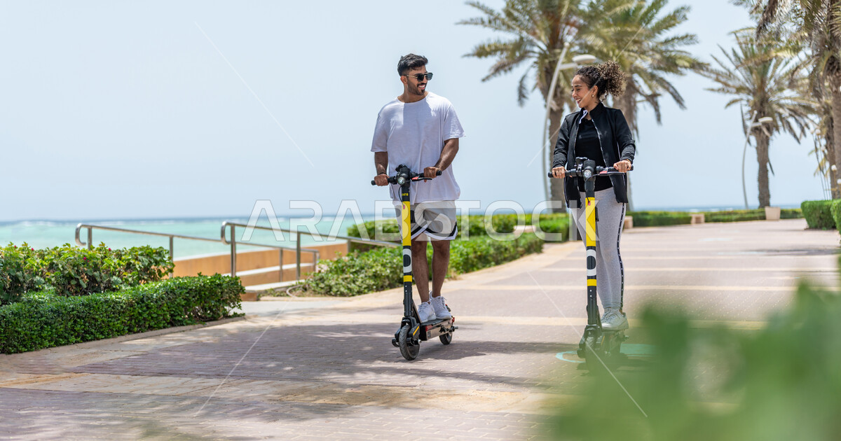 A Saudi Arabian Gulf man and woman riding an electric scooter in the