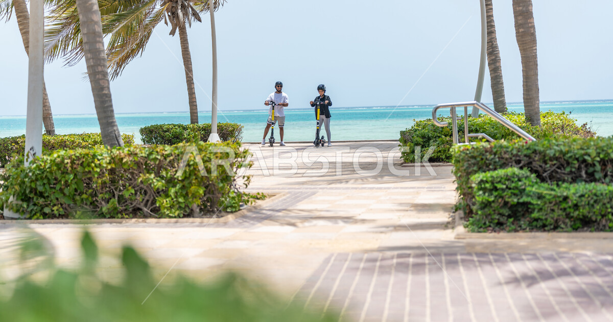 A Saudi Arabian Gulf man and woman riding an electric scooter in the