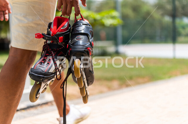 زاوية من الخلف لرجل عربي خليجي سعودي، يحمل بيده الزلاجات الدوارة في إحدى الحدائق الترفيهية بالسعودية، أماكن سياحية ترفيهية، قضاء أوقات ممتعة، أنشطة ترفيهية، ممارسة رياضة تزلج بالعجلات