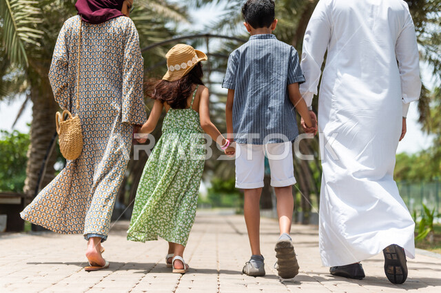 زاوية من الخلف لعائلة عربية خليجية سعودية تسير على طريق الممشى المخصص للمشي في إحدى الحدائق الترفيهية بالسعودية، فعاليات ترفيهية عائلية، عطلة صيفية، قضاء أوقات عائلية ممتعة، التنزه والترفيه، حدائق ونزهات ترفيهية للعائلة في المملكة العربية السعودية