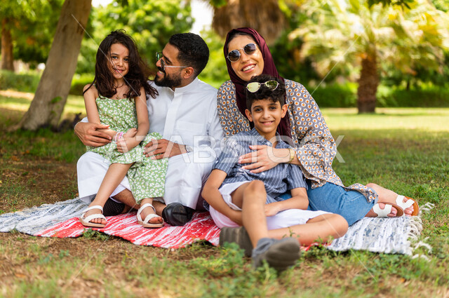 عائلة عربية خليجية سعودية تنظر إلى الكاميرا، تقضي أوقات ممتعة في إحدى الحدائق الترفيهية بالسعودية، فعاليات ترفيهية عائلية، عطلة صيفية، حدائق ونزهات ترفيهية للعائلة في المملكة العربية السعودية، أجواء عائلية سعيدة، قضاء أوقات عائلية ممتعة، التنزه والترفيه