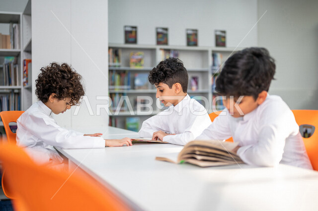 طلاب عرب سعوديون خليجيون يجلسون في المكتبة المدرسية، الاستمتاع بقراءة الكتب، مفهوم التعليم الذاتي, مكتبة المدرسة، بيئه مدرسيه تعليميه متطوره, المدارس المبتكره, جودة التعليم, مدارس أكاديميه في المملكة العربية السعودية