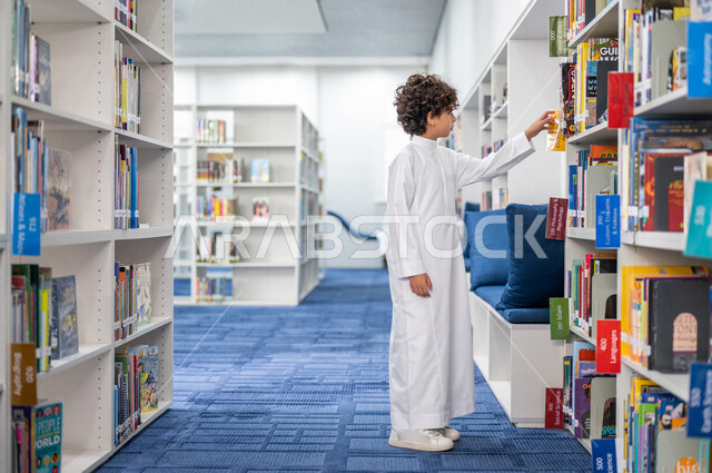 طالب عربي سعودي خليجي يقوم بإختيار كتاب من المكتبة المدرسية، الاستمتاع بقراءة الكتب، مفهوم القراءه والثقافه, مكتبة المدرسة، التعليم الذاتي, بيئه مدرسيه تعليميه متطوره, مدارس أكاديميه في المملكة العربية السعودية