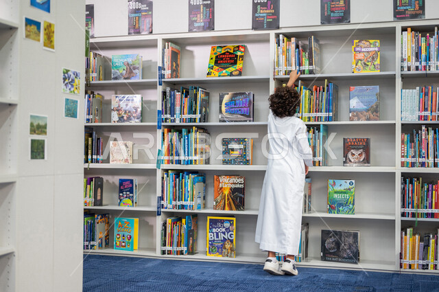 طالب عربي سعودي خليجي يقوم بإختيار كتاب من المكتبة المدرسية، الاستمتاع بقراءة الكتب، مفهوم القراءه والثقافه, مكتبة المدرسة، التعليم الذاتي, بيئه مدرسيه تعليميه متطوره, مدارس أكاديميه في المملكة العربية السعودية