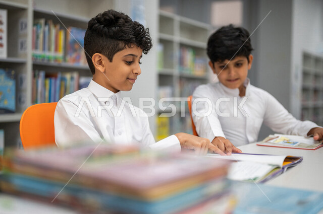 طالبان عربيان سعوديان خليجيان يجلسان في المكتبة المدرسية، الاستمتاع بقراءة الكتب، مفهوم التعليم الذاتي, مكتبة المدرسة، بيئه مدرسيه تعليميه متطوره, المدارس المبتكره, جودة التعليم, مدارس أكاديميه في المملكة العربية السعودية