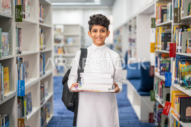 طالب عربي سعودي خليجي يحمل مجموعه من الكتب داخل المكتبة المدرسية، الاستمتاع بقراءة الكتب المدرسية، مفهوم التعليم والثقافه, مكتبة المدرسة، التعليم الذاتي, بيئه مدرسيه تعليميه متطوره, مدارس أكاديميه في المملكة العربية السعودية