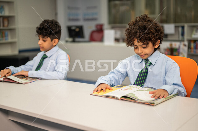 طالبان عربيان سعوديان خليجيان يجلسان في المكتبة المدرسية، الاستمتاع بقراءة الكتب، مفهوم التعليم الذاتي, مكتبة المدرسة، بيئه مدرسيه تعليميه متطوره, المدارس المبتكره, جودة التعليم, مدارس أكاديميه في المملكة العربية السعودية