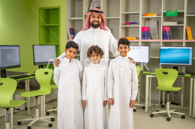 مجموعه من الطلاب العرب السعوديون الخليجيون يقفون مع المعلم في معمل الحاسوب, الترحيب بالطلاب الجدد, بيئه مدرسيه تعليميه متطوره, التعليم الذكي، المدارس المبتكره, جودة التعليم, مدارس أكاديميه في المملكه العربيه السعوديه
