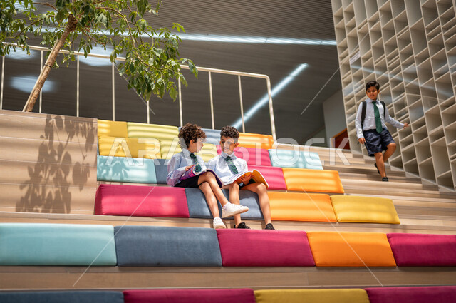 طالبان عربيان سعوديان خليجيان يجلسان على الأدراج في بهو المدرسه, المذاكره والمراجعه, الإستعداد للإمتحانات, بيئه مدرسيه تعليميه متطوره, التعليم الذكي, عالم جديد من التعليم، المدارس المبتكره, جودة التعليم, مدارس أكاديميه في المملكه العربيه السعوديه