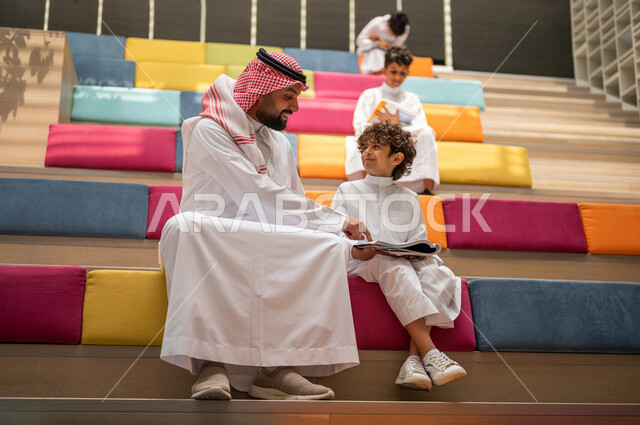 أستاذ عربي سعودي خليجي مع مجموعه من الطلاب يجلسون على الأدراج في بهو المدرسه, المذاكره والمراجعه, الإستعداد للإمتحانات, بيئه مدرسيه تعليميه متطوره, التعليم الذكي, عالم جديد من التعليم، المدارس المبتكره, جودة التعليم, مدارس أكاديميه في السعوديه