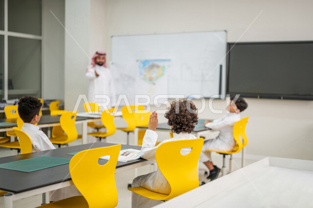 A Saudi Arabian Gulf teacher in an advanced educational school environment, following up a group of students in the classroom, Montessori education system, smart education, a new world of education, promoting science and innovation, skills development, in