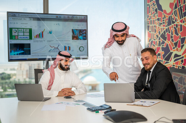 فريق عمل سعودي ورجل بالبدلة الرسمية في غرفة الإجتماعات داخل مقر الشركة، إستخدام جهاز الحاسوب المحمول، مهن ووظائف سعودية، شركة سعودية، بيئة عمل، زملاء عمل، ورشة أعمال، الشراكة والتعاون، إجتماع عمل، مناقشة ومتابعة أهداف الشركة