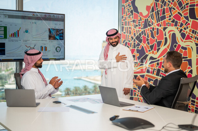 فريق عمل سعودي ورجل بالبدلة الرسمية في غرفة الإجتماعات داخل مقر الشركة، التصفيق والتشجيع، مهن ووظائف سعودية، شركة سعودية، بيئة عمل، زملاء عمل، ورشة أعمال، الشراكة والتعاون، إجتماع عمل، النجاح وتحقيق الأهداف