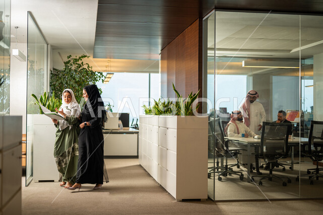 موظفتان عربيتان سعوديتان خليجيتان داخل مقر الشركة، ترتديان عبايات عصرية مميزة، أزياء محجبات، مهن و وظائف سعودية، شركة سعودية، سيدات أعمال، الحوارات والنقاشات، بيئة العمل، دردشة عمل، غرفة إجتماعات، متابعة ومناقشة الأعمال