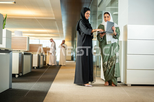 موظفتان عربيتان سعوديتان خليجيتان داخل مقر الشركة، ترتديان عبايات عصرية مميزة، إستخدام جهاز الحاسوب المحمول، مهن و وظائف سعودية، شركة سعودية، سيدات أعمال، الحوارات والنقاشات، بيئة العمل، دردشة عمل، متابعة ومناقشة الأعمال