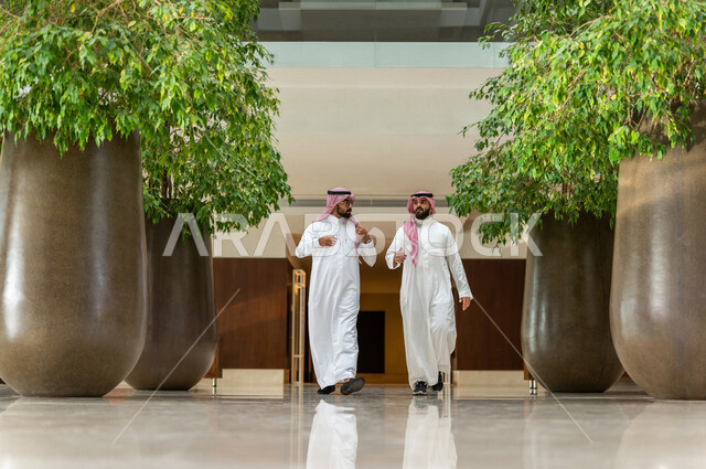 Two Saudi Arabian Gulf employees inside the company’s headquarters, wearing traditional Saudi dress, Saudi professions and jobs, Saudi company, businessmen, dialogues and discussions, work environment, work chat, co-workers