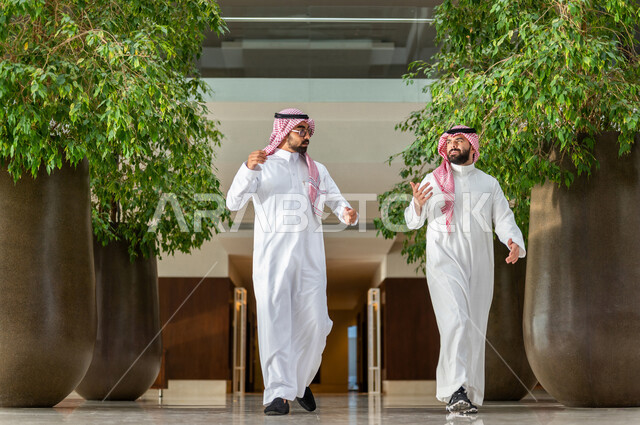 موظفان عربيان سعوديان خليجيان داخل مقر الشركة ، يرتديان الزي السعودي التقليدي، مهن و وظائف سعودية ، شركة سعودية ، رجال أعمال ، الحوارات والنقاشات ، بيئة العمل ، دردشة عمل ، زملاء عمل