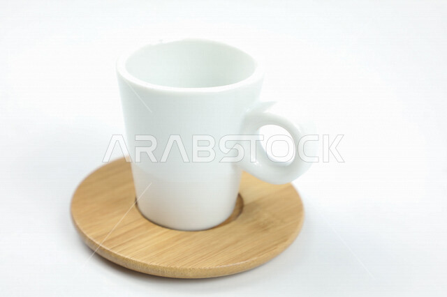 صورة مقربة لكوب ابيض اللون، فنجان ابيض فارغ، طبق خشبي، كوب زجاجي على قاعدة خشبية، خلفية بيضاء