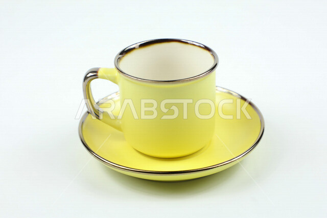 صورة مقربة لكوب اصفر اللون، فنجان اصفر فارغ، طبق صغير، كوب زجاجي، خلفية بيضاء