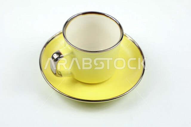 صورة مقربة لكوب اصفر اللون، فنجان اصفر فارغ، طبق صغير، كوب زجاجي، خلفية بيضاء