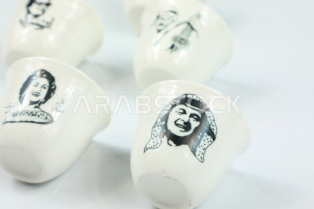 صورة مقربة لمجموعة من الفناجين الصغيرة، فنجان مزخرف برسومات ابداعية لمجموعة من الفنانيين، اكواب بيضاء فارغة، كوب ضيافة صغير، كوب زجاجي، خلفية بيضاء