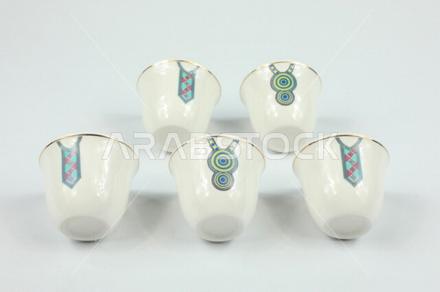 صورة مقربة لمجموعة من الفناجين الصغيرة، فنجان مزخرف برسومات ابداعية، اكواب بيضاء فارغة، كوب ضيافة صغير، كوب زجاجي، خلفية بيضاء